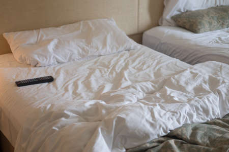 TV remote control on messy bed in hotel bedroomの写真素材