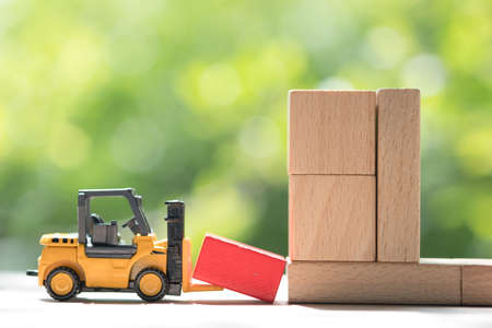 Mini forklift truck load red wooden block to complete building with natural green background. Industry concept.の写真素材