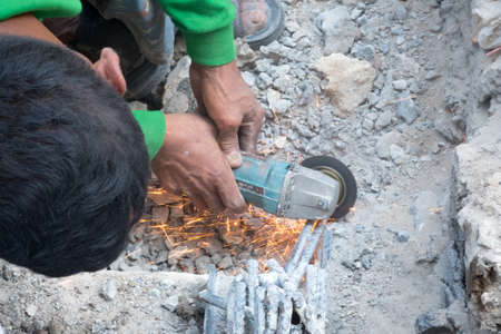 The hands of worker cut metal iron with a grinding machine. orange sparks fly from grinding machine...