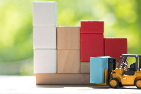 Mini forklift truck load blue wooden block to complete building with natural green background....