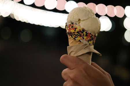 Hand holding vanilla ice cream with bokeh light and blurred in night