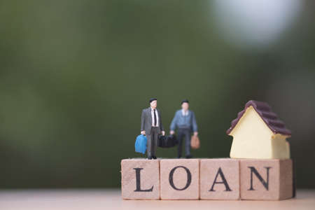 Miniature people businessman standing with wood word LOAN and blurred green nature as background....