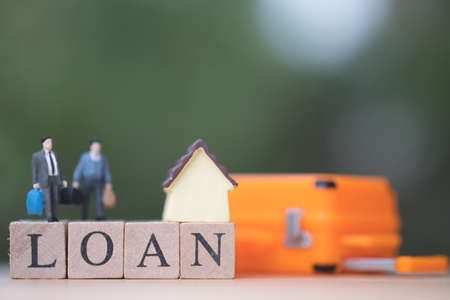 Miniature people businessman standing with wood word LOAN and blurred green nature as background. Trading house conceptの写真素材