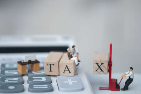 Miniature people businessman sit on wood word TAX placed on calculator. Pay annual income (TAX) for the year. using as background business concept and finance conceptの写真素材