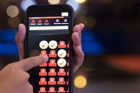 Hand holding smartphone with booking button and seat icon on screen. Mobile application for online buy cinema tickets. Concept of hotel booking onlineの写真素材