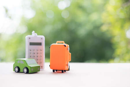 Miniature toy car and miniature orange suitcases with calculator on nature background. Concept of travel or travel insurance or vacationの写真素材