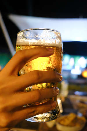 Hand holding a glass of beer with bokeh backgroundの写真素材