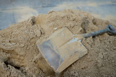 Close up view spade stained with cement and concrete lies on a pile of sand.の写真素材