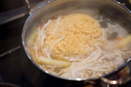 Boiled instant noodles and enoki mushroom in hot soup, selective focus. Instant noodles is a convenient, delicious and cheap food.の写真素材