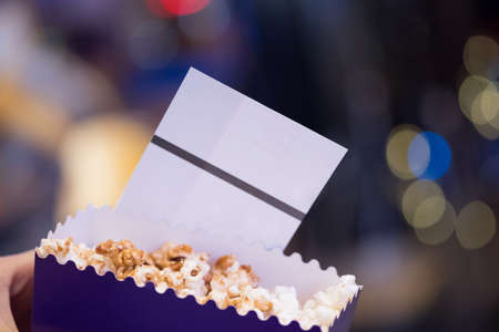 Movie tickets and bucket of popcorn in hand, concept of leisureの写真素材