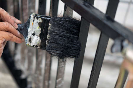 Hand with paintbrush painting iron fence with black paint. Concept of renovation houseの写真素材