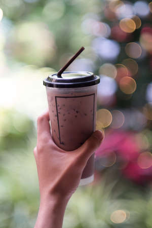 Hand holding iced chocolate or cacao in glass with blur light background