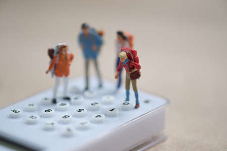 Miniature people backpacker standing on white calculator for calculate money and time to travel. Concept of travel planning and save costの写真素材