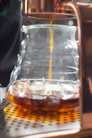 Close up image of a drip coffee dropping into a beaker on wooden tableの写真素材