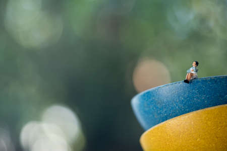 Miniature people, woman sitting on blue cup on green nature background, concept of wife rest after hard workの写真素材