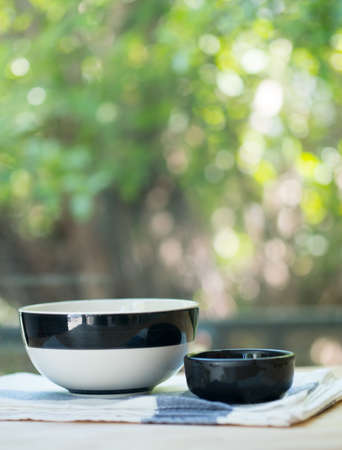 Black and white bowls on napkin on table with nature blur backgroundの写真素材