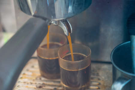 Close up of espresso pouring from coffee machine to shot glass. Professional coffee brewingの写真素材