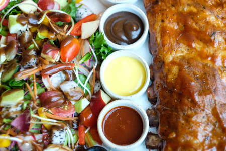 Roasted pork ribs with barbecue sauce and fruit salad served with three salad dressingの写真素材