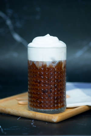 Ice chocolate in a tall glass with milk foam on top. Cold summer drink