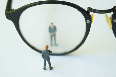 Miniature businessman standing looking through glasses, using as background business concept with...