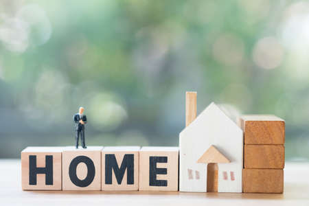 Miniature people stand on wood block words HOME with wood home.  Depicts a property related business.の写真素材
