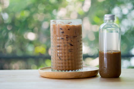 Iced coffee mocha in a tall glass and bottle on table