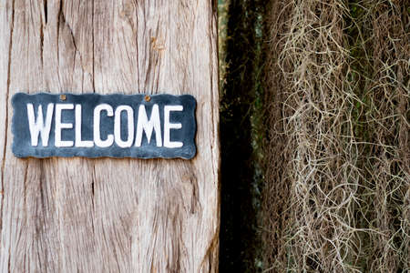 Welcome text on wooden tag hanging on wooden wall in home or shopの写真素材