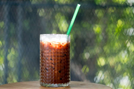 Tasty chocolate drink in tall glass cup on nature green background