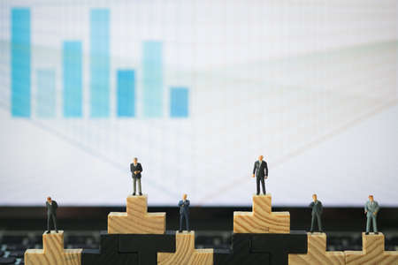 Miniature people: Each businessmen are standing on wood block in different position with graph...