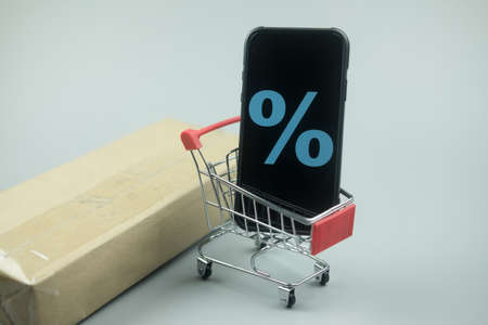 Smartphone with discount sign on screen in a shopping cart. Concept of online shopping, E commerce and delivery of goods.の写真素材