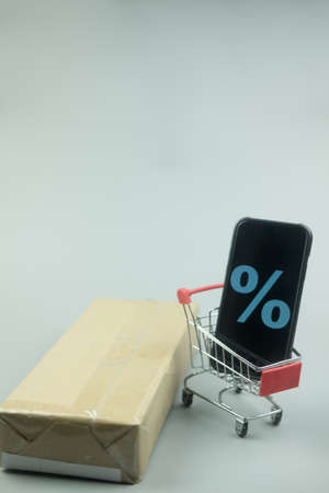 Smartphone with discount sign on screen in a shopping cart. Concept of online shopping, E commerce and delivery of goods.の写真素材