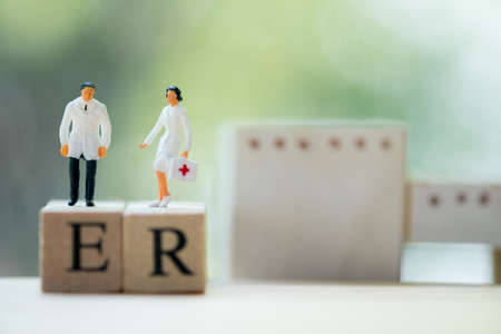 Miniature people: Doctor and nurse standing on wooden block with words ER. Health care and emergency concept.の写真素材