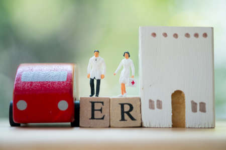 Miniature people: Doctor and nurse standing on wooden block with words ER, car and hospital. Concept...