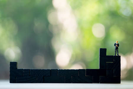 Miniature people: Businessman standing on black wooden puzzle pieces. Concept of businessの写真素材