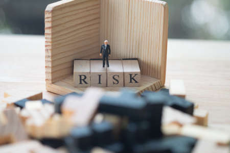 Miniature people : businessman standing on a wood cube word with risk. Business risk assessment or management conceptの写真素材
