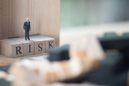 Miniature people : businessman standing on a wood cube word with risk. Business risk assessment or...