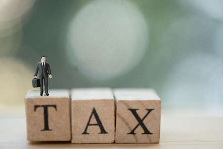 Miniature businessman standing on wood words TAX. Concept of pay annual income (TAX)の写真素材