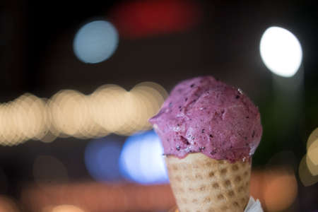 Blueberry ice cream in waffle cone on young man hand with light night background