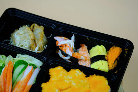 Fresh food portion in Japanese bento box with sushi rolls, salad and main course. Top View