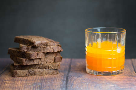 Sliced dark brown bread made of rye and wheat flour on wood table and fresh orange juice