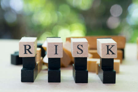 Cube wooden block with alphabet building the word RISK. Decision to accept business result in uncertaintyの写真素材