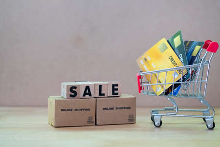 Wooden block word SALE put on miniature brown boxes near cart shopping and credit card inside....