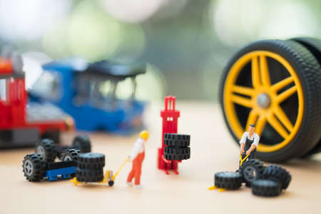 Miniature people : Handsome mechanic in uniform is examining a tire working in auto service. Concept...