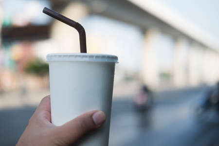 White paper cups with drinking straw takeaway drinks in hand. Male hand is holding paper cup