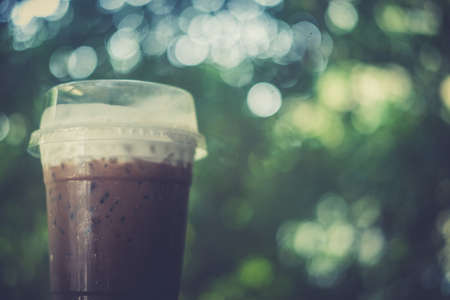 Iced coffee mocha with foam milk in plastic glass on nature blur backgroundの写真素材