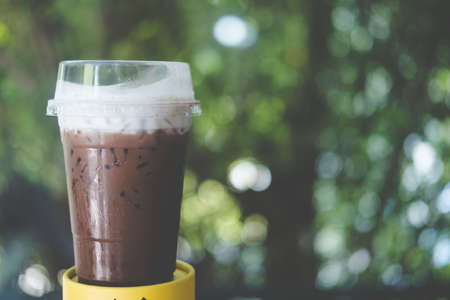 Iced coffee mocha with foam milk in plastic glass on nature blur background