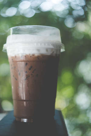 Iced coffee mocha with foam milk in plastic glass on nature blur background