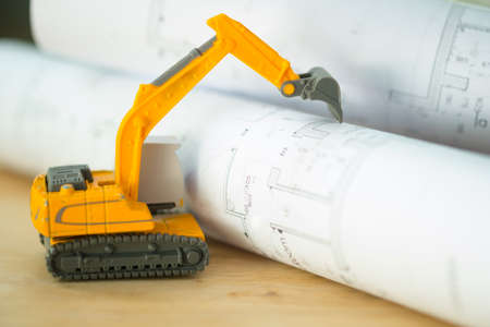 Heavy duty construction backhoe toy with house plan blueprints. Concept of demolition of building.の写真素材