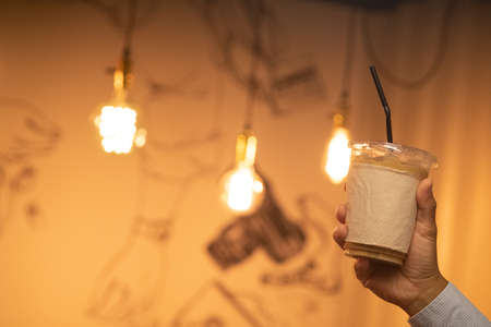 Hand holding iced latte with straw in plastic cup in cafe restaurant