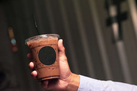 Businessman hand holding iced mocha with straw in plastic cupの写真素材